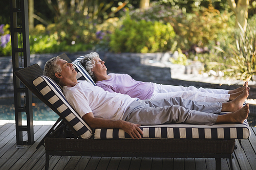 Full length of senior couple resting together on lounge chairs at porch