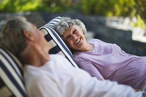 Smiling senior woman looking at man resting together on lounge chairs