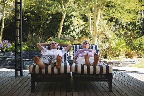 Full length of senior couple resting on lounge chairs at porch