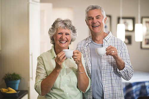 Portrait of happy senior couple holding cups in kitchen at home