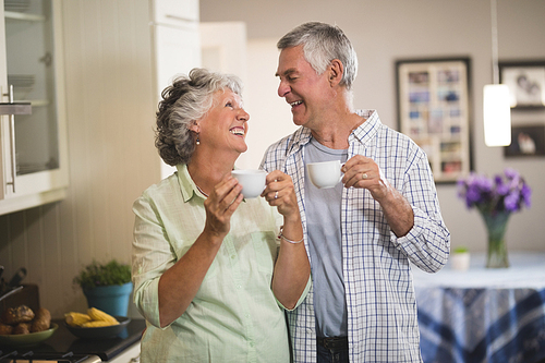 Happy senior couple looking at each other while holding cups in kitchen
