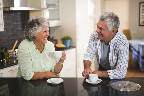 Cheerful senior couple looking at each other while having coffee at home