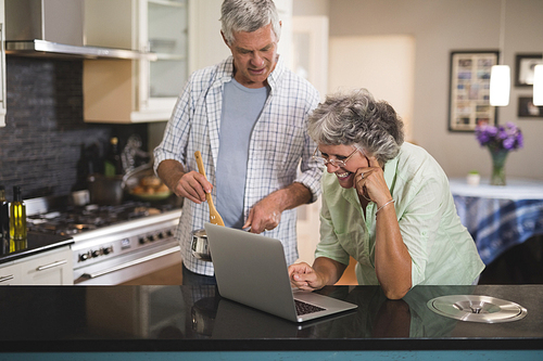 Smiling senior woman using laptop with husband in kitchen at home