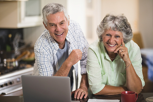 Portrait of smiling couple with laptop in kitchen at home