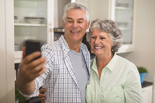 Cheerful senior couple taking selfie in kitchen at home