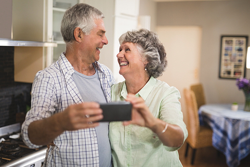 Cheerful senior couple with mobile phone in kitchen at home