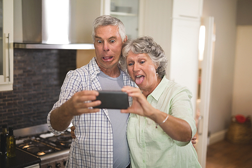 Mischievous senior couple taking selfie in kitchen at home