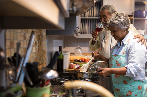 Man having wine while woman preparing food in kitchen at home