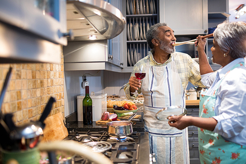 Woman feeding man while standing in kitchen at home