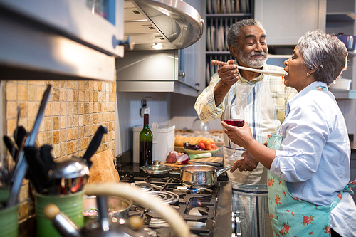 Man feeding woman while standing in kitchen at home