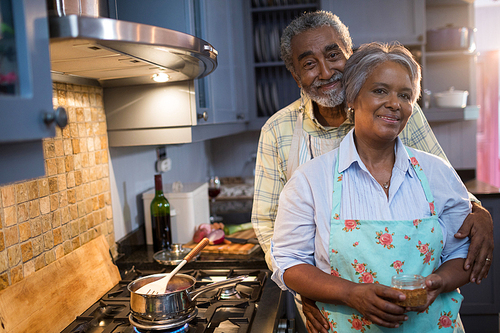 Portrait of couple standing by stove in kitchen at home