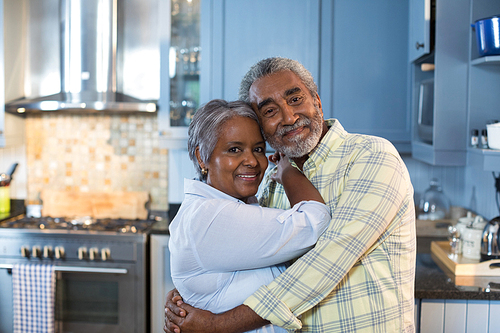 Portrait of affectionate couple embracing while standing in kitchen at home