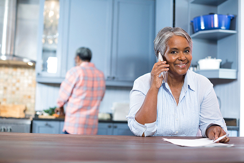 Portrait of smiling woman talking phone while standing in kitchen at home