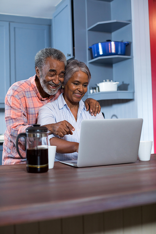 Smiling couple using laptop in kitchen at home