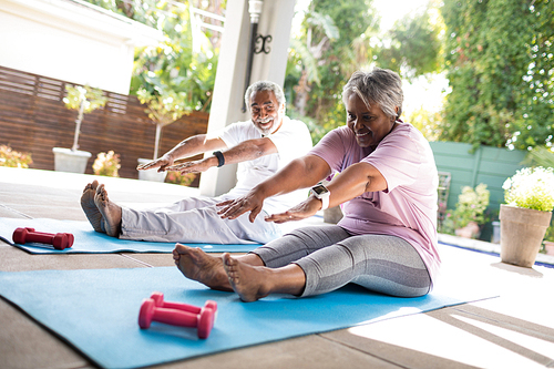 Full length of senior couple doing stretching exercise while sitting on exercise mat in yard
