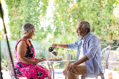 Senior man pouring coffee while sitting at table with woman in yard