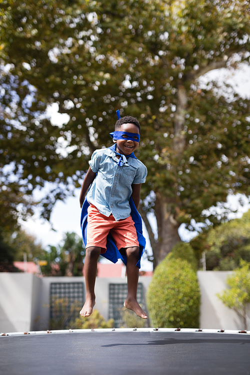 Full length of boy in superhero costume jumping on trampoline