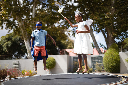 Siblings in costumes jumping on trampoline at lawn