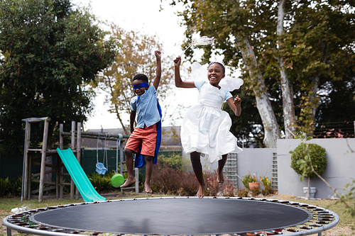 Playful siblings in costumes enjoying on trampoline at lawn