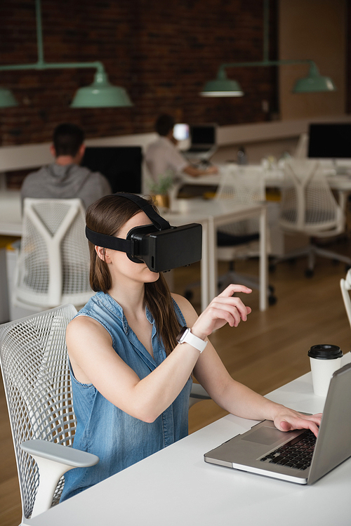 Female executive using virtual reality headset while using laptop in office