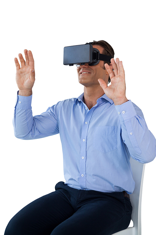 Smiling businessman with vr glasses gesturing while sitting on chair against white background
