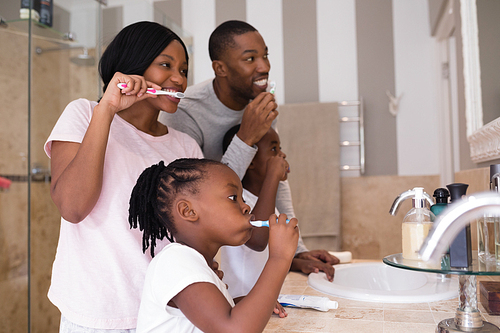 Happy parents with children brushing teeth in bathroom at home