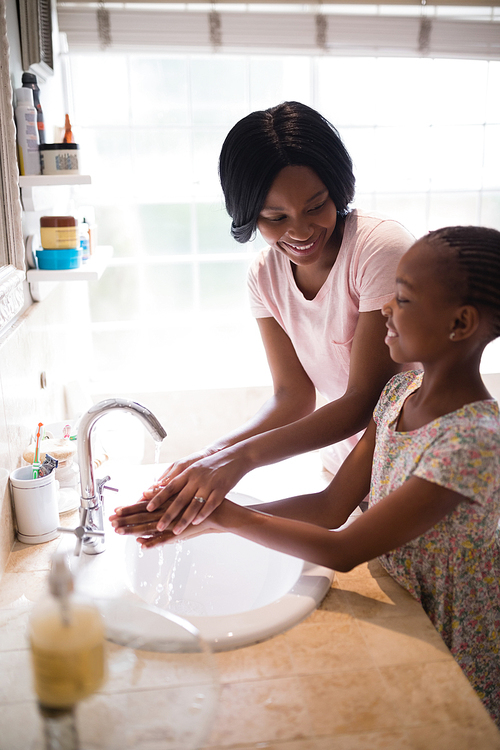 Smiling mother looking at daughter while washing hands in bathroom