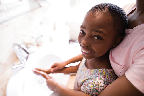 Mid section of mother assisting daughter while washing hands in bathroom