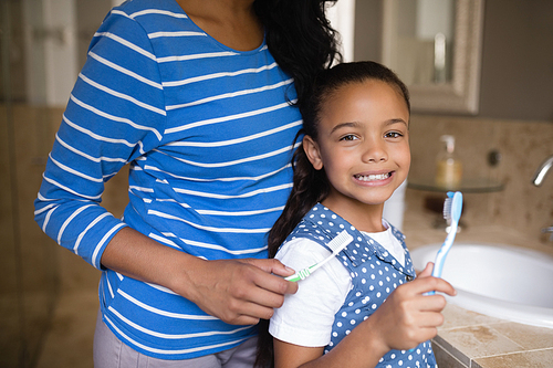 Portrait of smiling girl with mother brushing teeth in bathroom