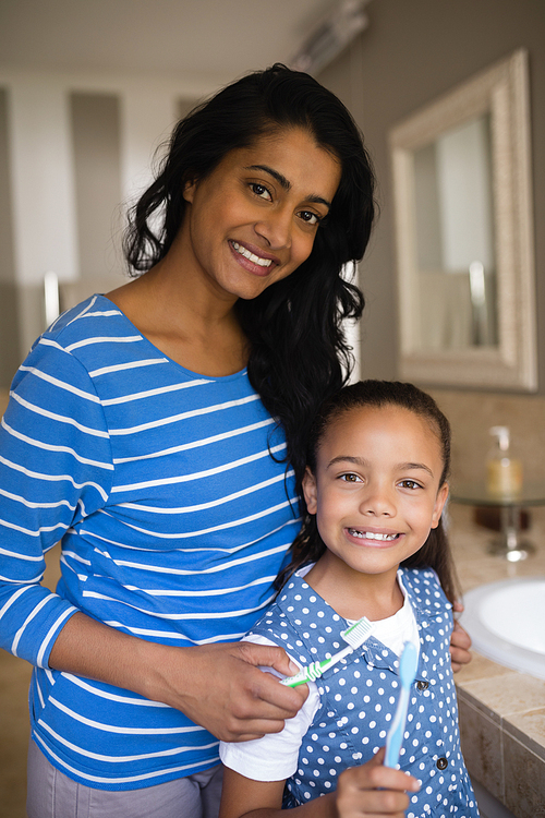 Portrait of smiling girl with mother holding toothbrushes in bathroom