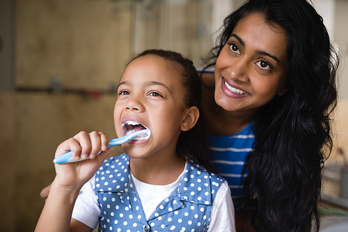 Smiling mother standing by daughter brushing teeth in bathroom at home