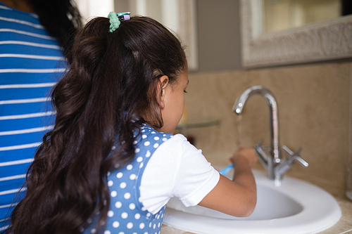 Rear view of girl with mother brushing teeth at bathroom sink
