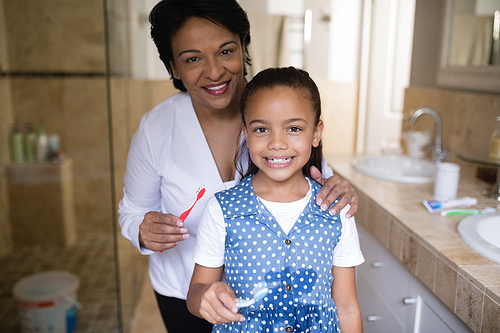 Portrait of smiling girl with grandmother holding toothbrushes in bathroom
