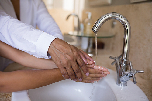 Mid section of granny helping girl while washing hands at sink in bathroom