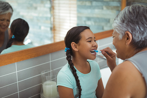 Grandmother helping granddaughter brush her teeth in the bathroom at home