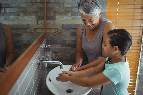Grandmother and granddaughter washing hands in bathroom sink at home