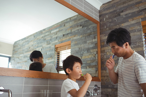 Father and son brushing teeth together in bathroom at home