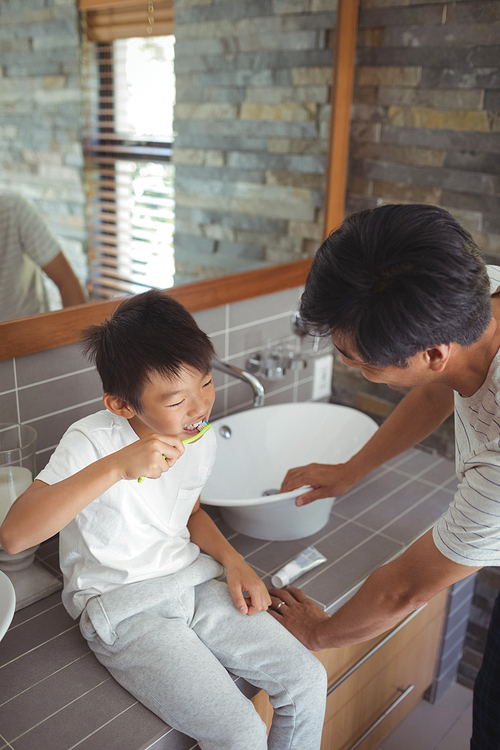 Son brushing his teeth with father in bathroom at home