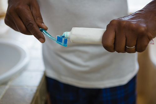 Mid section of man applying toothpaste on brush in bathroom at home