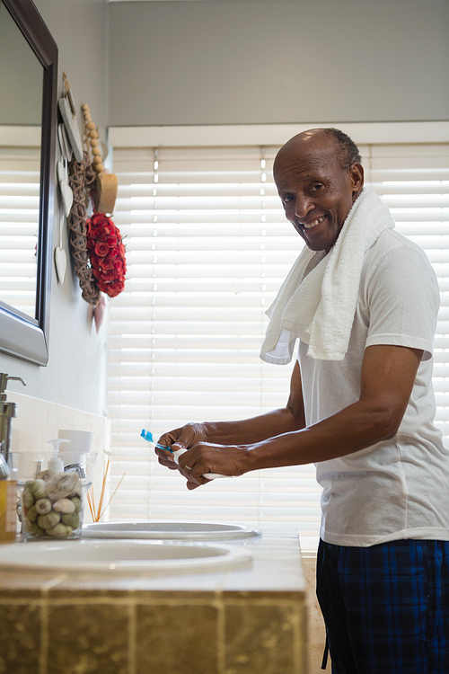 Portrait of smiling senior man standing by sink in bathroom at home