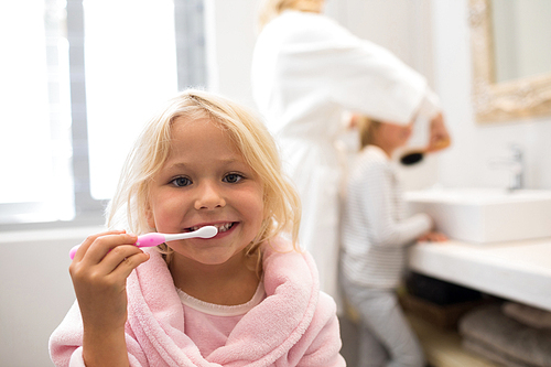 Portrait of girl brushing teeth in bathroom