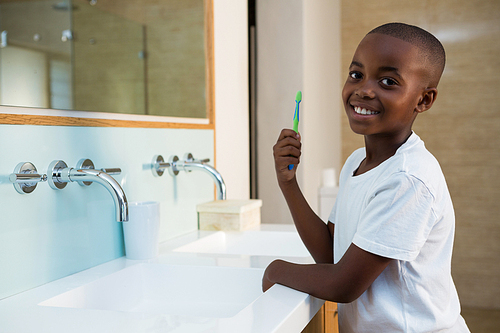 Side view of portrait of smiling boy with toothbrush standing in bathroom