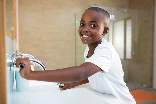 Side view portrait of smiling boy with toothbrush looking at mirror in domestic bathroom