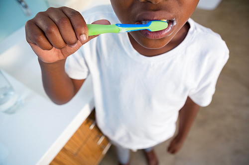 Midsection of boy brushing teeth by sink at bathroom