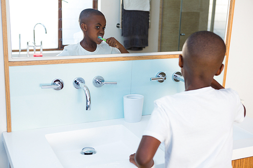 Boy brushing teeth looking at mirror reflection at domestic bathroom