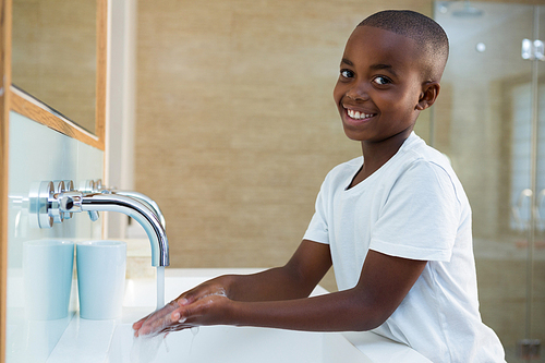 Portrait of smiling boy washing hands in sink at bathroom