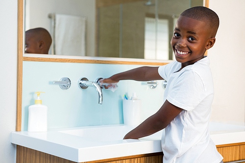 Side view portrait of smiling boy washing hands in sink at domestic bathroom