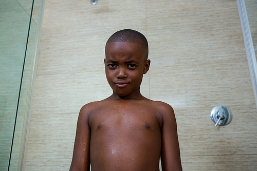 Low angle portrait of shirtless boy standing against tiled wall at bathroom