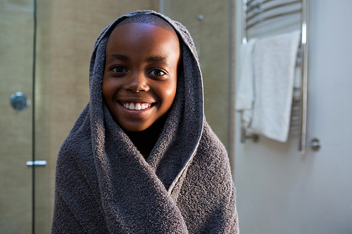 Portrait of smiling boy wrapped in gray towel at domestic bathroom