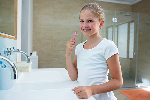 Portrait of girl holding toothbrush while standing in bathroom